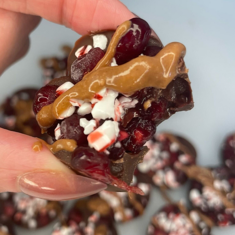 Close-up of pomegranate chocolate bite with pomegranate seeds, cashew butter drizzle and peppermint pieces on pale blue background