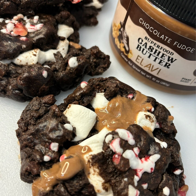 Close-up of Hot Cocoa cookie with melted ELAVI Chocolate Fudge cashew butter, marshmallows and peppermint flakes, jar behind