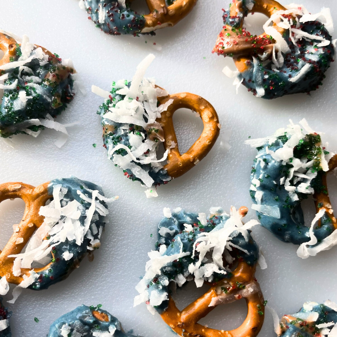 Top-down view of Blue Magic dipped pretzels showcasing blue frosting coating with shredded coconut flakes and red-green sprinkles on a white board
