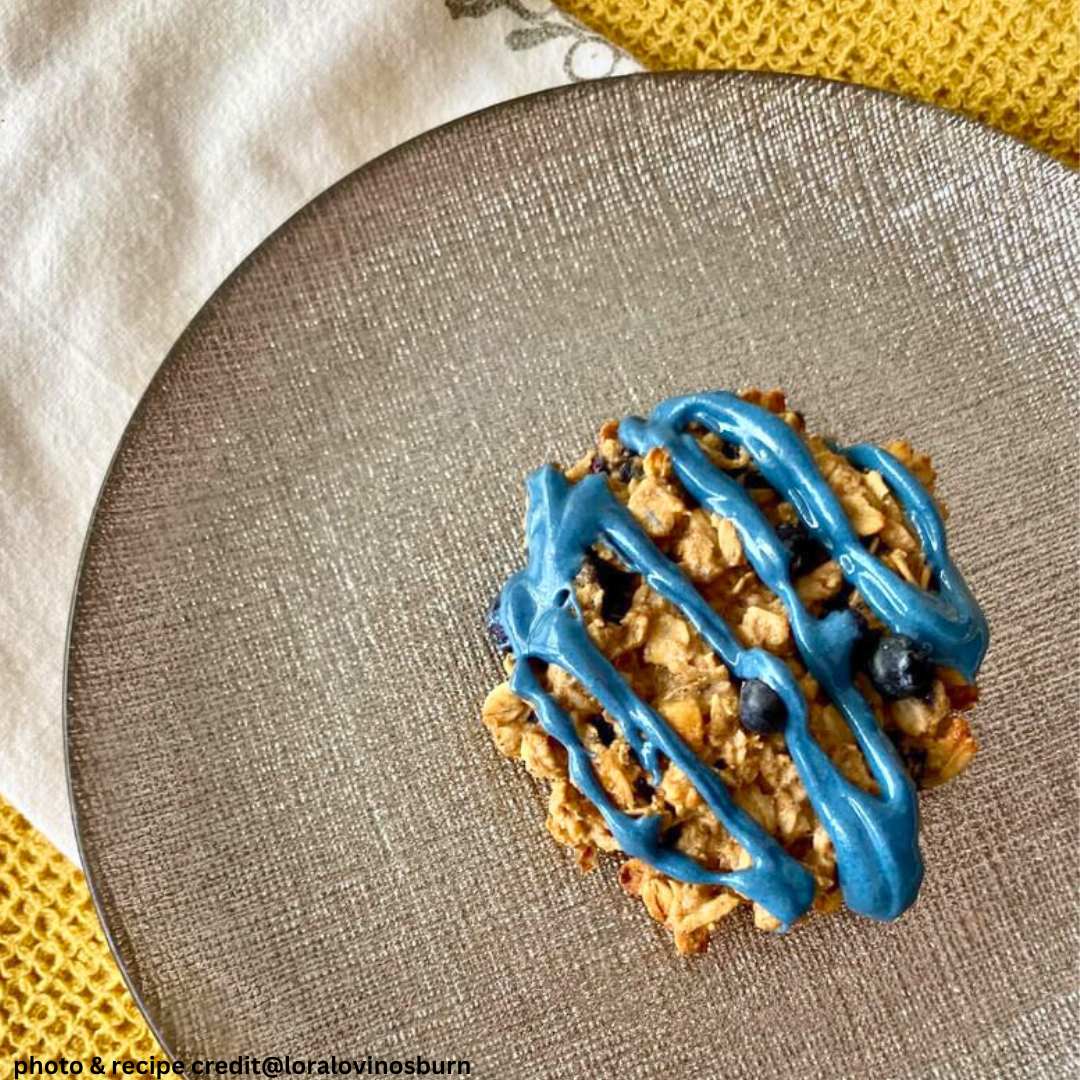 Overhead view of blueberry breakfast cookie with blue vanilla frosting drizzle and fresh blueberries on a textured gray plate