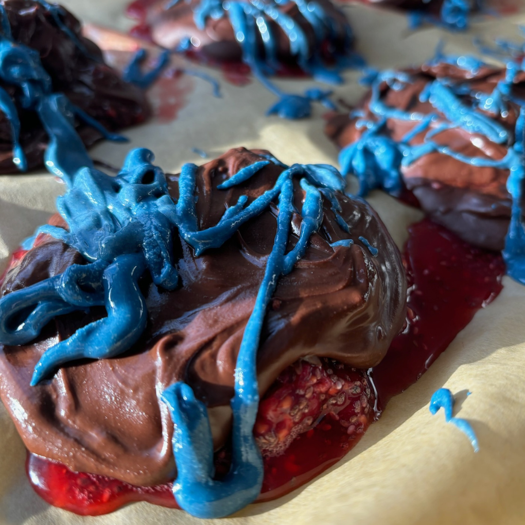 Close up of Raspberry Chia Bites with chocolate-coated frozen raspberries drizzled in blue vanilla frosting on parchment