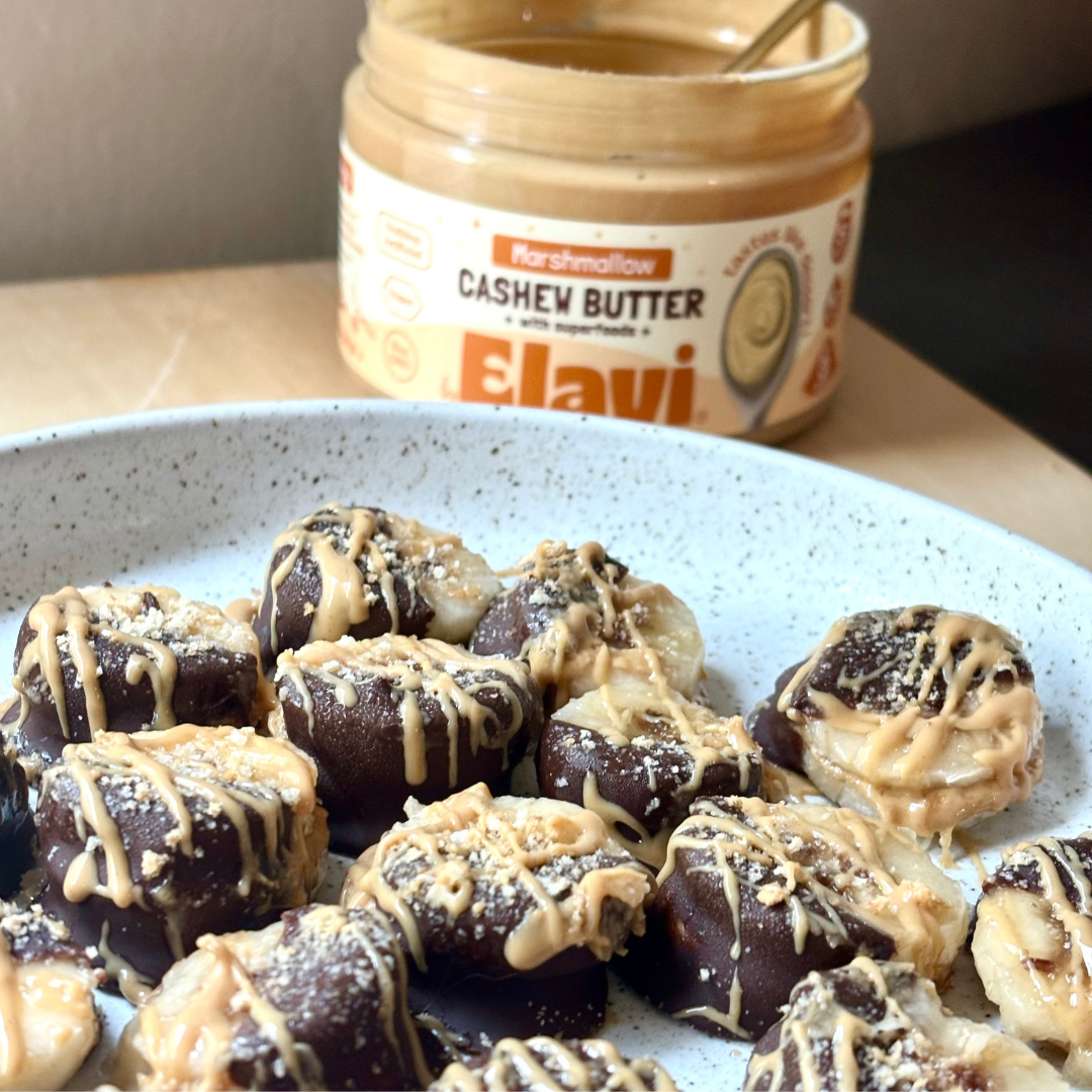 Banana s’mores bites dipped in chocolate and drizzled with marshmallow cashew butter on a speckled plate, jar in background