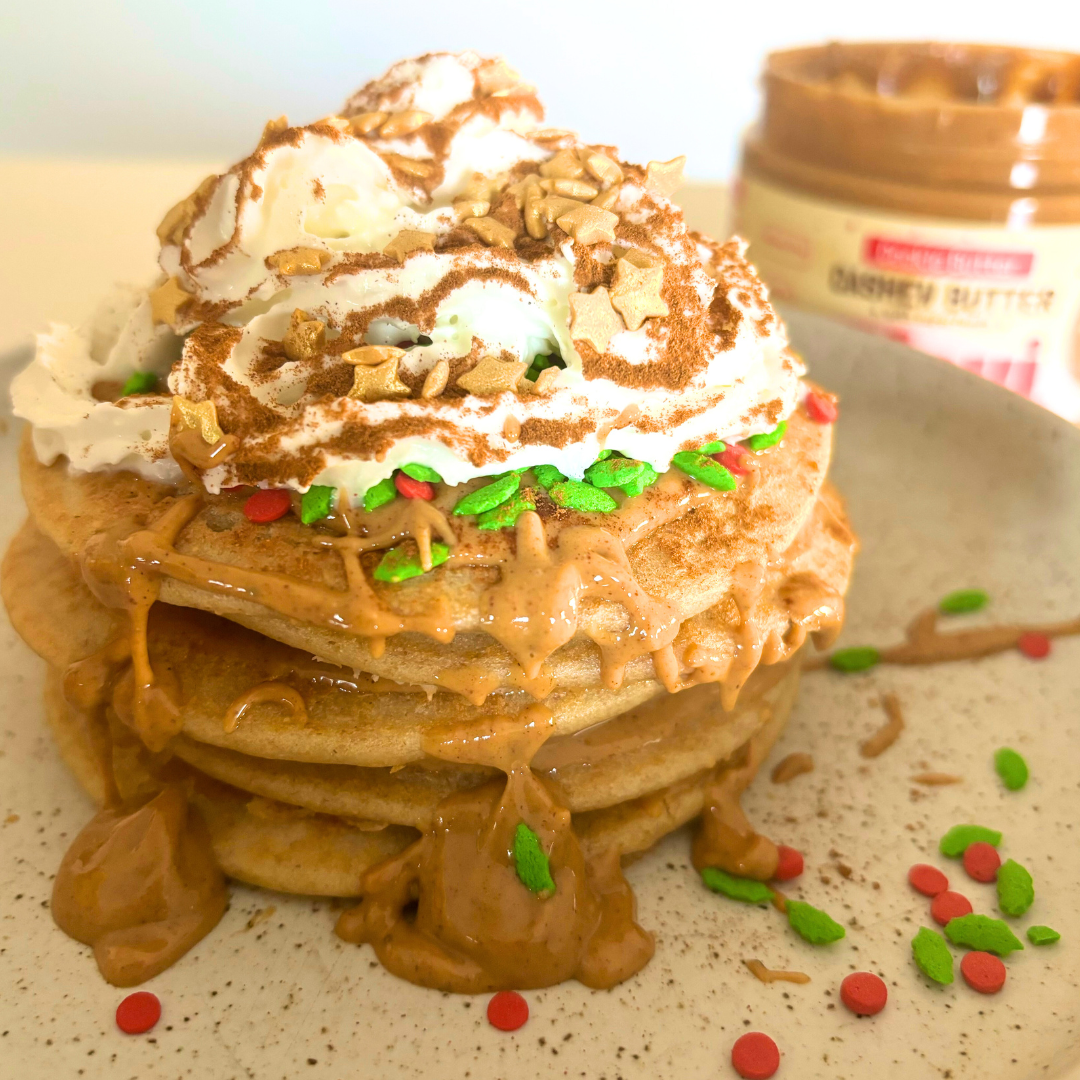 Protein pancakes drizzled with cookie butter, topped with whipped cream and red-and-green sprinkles, jar in background