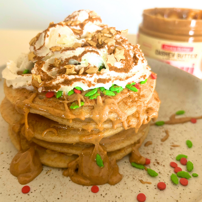 Protein pancakes drizzled with cookie butter, topped with whipped cream and red-and-green sprinkles, jar in background
