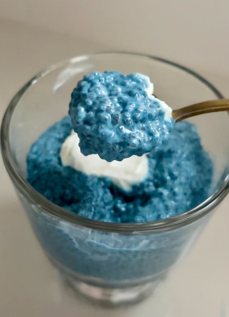 Close-up of blue spirulina chia pudding in a clear glass showcasing a spoonful of textured pudding and a dollop of yogurt