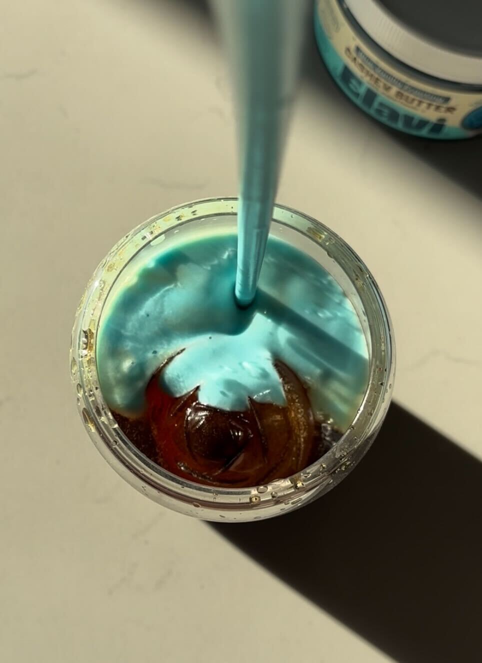 Top-down view of Elavi blueberry cold brew showing bright blue foam, ice, and a straw on a light countertop