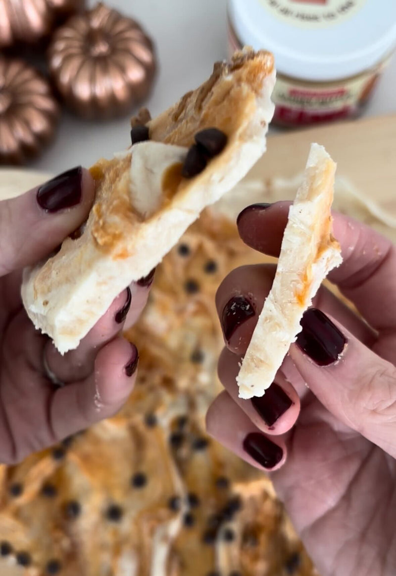 Close-up of pumpkin spice yogurt bark broken in hands showing creamy bark with pumpkin swirl and chocolate chips