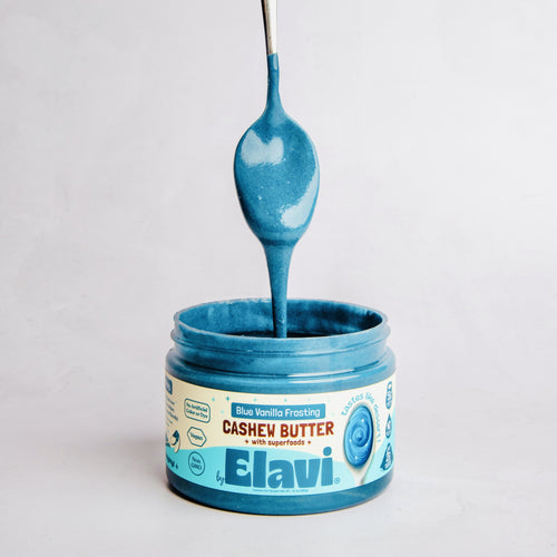 Front of Blue Vanilla Frosting cashew butter jar with spoon dripping blue frosting and Elavi branding on light gray