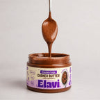 Close-up of Chocolate Fudge cashew butter jar with spoon lifting glossy, smooth spread against a plain light background