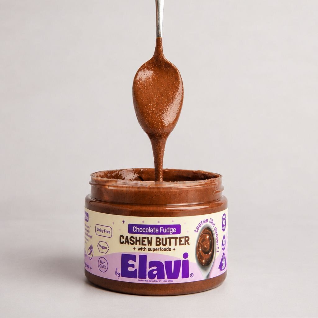 Close-up of Chocolate Fudge cashew butter jar with spoon lifting glossy, smooth spread against a plain light background